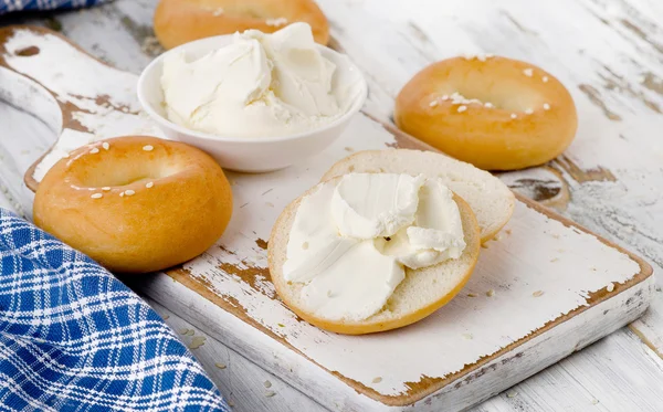 Bagels with cream cheese on a white wooden table. — Stock Photo, Image