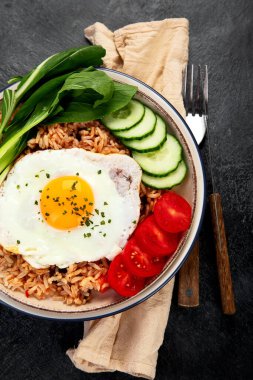 Bir tabak Nasi Goreng, pilav, sebze ve koyu arkaplanda bir yumurta. Üst görünüm.