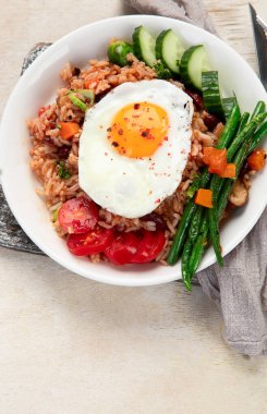 Bir tabak Nasi Goreng, pilav, sebze ve açık arkaplanda bir yumurta. Üst görünüm.