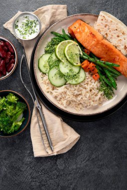 Kızarmış somon balığı filetosu, pilav, sebze ve limonla birlikte koyu bir arka planda. Üst görünüm.