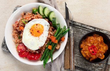 Bir tabak Nasi Goreng, pilav, sebze ve açık arkaplanda bir yumurta. Üst görünüm.