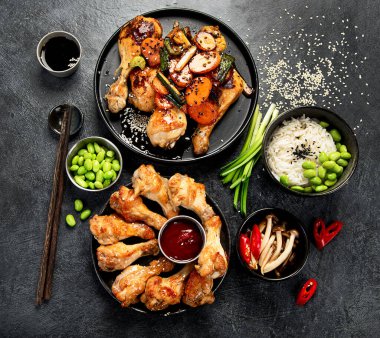 Masada çeşitli tavuk tabakları: tatlı ve ekşi tavuk tabağı, koyu arkaplanda kırmızı biber soslu tavuk bacağı. Üst görünüm.