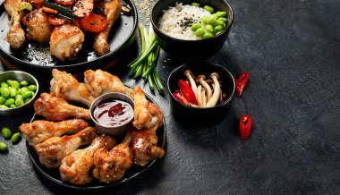 Masada çeşitli tavuk tabakları: tatlı ve ekşi tavuk tabağı, koyu arkaplanda kırmızı biber soslu tavuk bacağı. Üst görünüm.