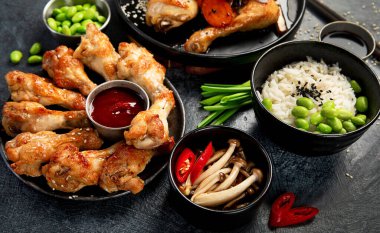 Masada çeşitli tavuk tabakları: tatlı ve ekşi tavuk tabağı, koyu arkaplanda kırmızı biber soslu tavuk bacağı. Üst görünüm.