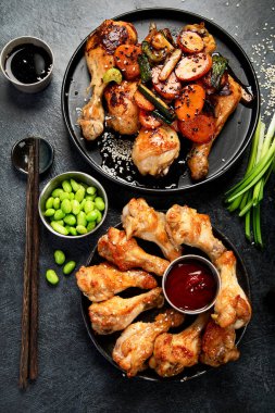 Masada çeşitli tavuk tabakları: tatlı ve ekşi tavuk tabağı, koyu arkaplanda kırmızı biber soslu tavuk bacağı. Üst görünüm.