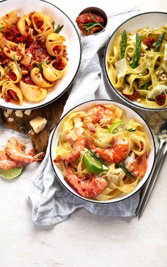 İtalyan makarnası. Etli domates soslu spagetti, deniz ürünleri makarnası, arka planda vejetaryen makarna. Üst görünüm.