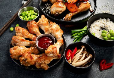 Masada çeşitli tavuk tabakları: tatlı ve ekşi tavuk tabağı, koyu arkaplanda kırmızı biber soslu tavuk bacağı. Üst görünüm.