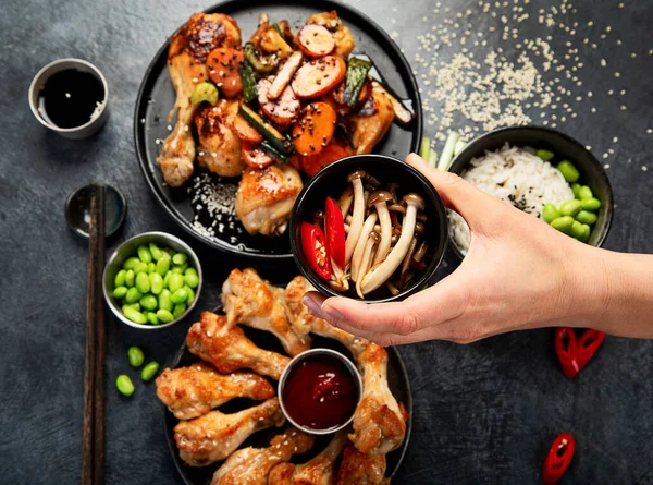 Masada çeşitli tavuk tabakları: tatlı ve ekşi tavuk tabağı, koyu arkaplanda kırmızı biber soslu tavuk bacağı. Üst görünüm.