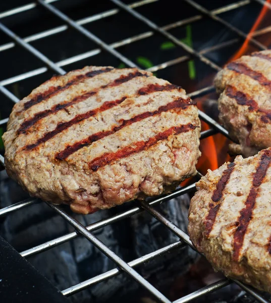 Hamburgers pasteitjes over vlammen op een grill. — Stockfoto