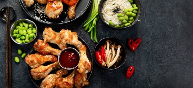 Masada çeşitli tavuk tabakları: tatlı ve ekşi tavuk tabağı, koyu arkaplanda kırmızı biber soslu tavuk bacağı. Üst görünüm.