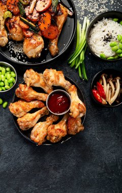 Masada çeşitli tavuk tabakları: tatlı ve ekşi tavuk tabağı, koyu arkaplanda kırmızı biber soslu tavuk bacağı. Üst görünüm.