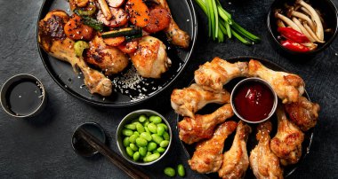 Masada çeşitli tavuk tabakları: tatlı ve ekşi tavuk tabağı, koyu arkaplanda kırmızı biber soslu tavuk bacağı. Üst görünüm.