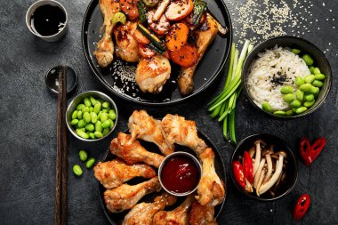 Masada çeşitli tavuk tabakları: tatlı ve ekşi tavuk tabağı, koyu arkaplanda kırmızı biber soslu tavuk bacağı. Üst görünüm.