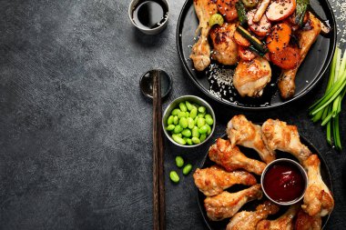 Masada çeşitli tavuk tabakları: tatlı ve ekşi tavuk tabağı, koyu arkaplanda kırmızı biber soslu tavuk bacağı. Üst görünüm.