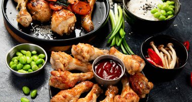 Masada çeşitli tavuk tabakları: tatlı ve ekşi tavuk tabağı, koyu arkaplanda kırmızı biber soslu tavuk bacağı. Üst görünüm.