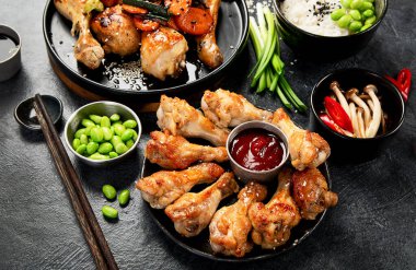 Masada çeşitli tavuk tabakları: tatlı ve ekşi tavuk tabağı, koyu arkaplanda kırmızı biber soslu tavuk bacağı. Üst görünüm.