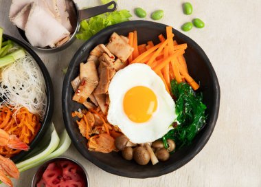 Lezzetli bimbimbap Kore pilavı sığır yumurtalı yumurta sarısı, susamlı havuç turşusu hafif arka planda geleneksel baharatlı yemekler. Üst görünüm.