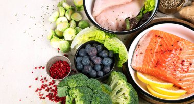 Hafif arka planda pek çok farklı sağlıklı yiyecek. Taze sebze, et, balık, tahıl ve meyve. Üst görünüm.