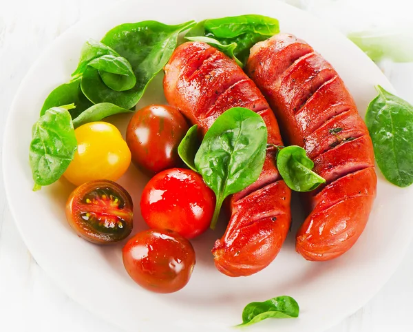 Kızarmış sosis ve domates beyaz bir plaka üzerinde.