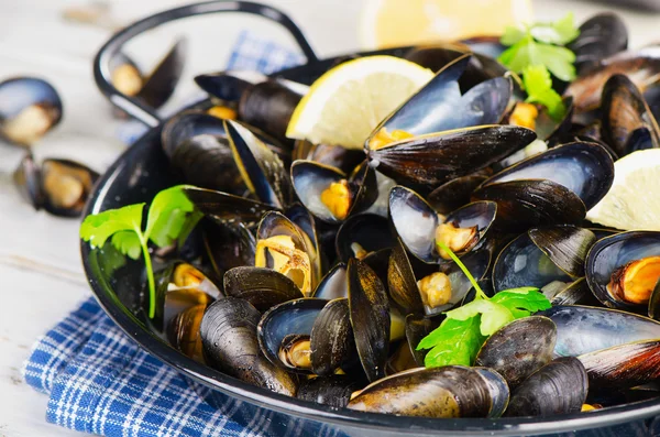 Copper pot of mussels garnished with lemon and herbs. — Stock Photo, Image