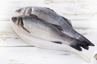 Two raw seabass on a board clipart