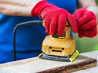 Kırmızı eldivenli kadın elleri zımpara makinesiyle tahtayı zımparalıyor. 