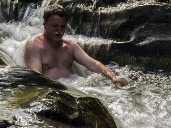 Hombre de mediana edad nadando en una cascada — Foto de Stock