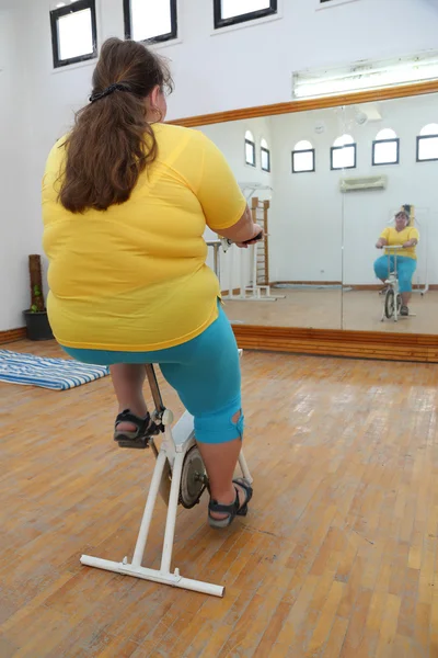 自転車シミュレーターで運動する太りすぎの女性 — ストック写真