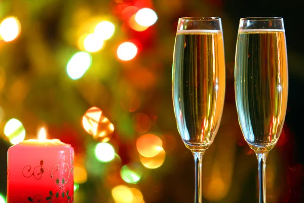 Glasses with champagne and candle against festive lights — Stock Photo, Image