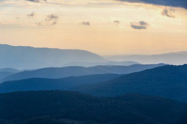 Ukrayna 'daki Karpat Dağları' nın günbatımı manzarası. Karpat sırasının katmanlı mavi sırtları batan güneşin yumuşak altın parıltısıyla yıkandı.