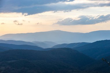 Ukrayna 'daki Karpat Dağları' nın günbatımı manzarası. Karpat sırasının katmanlı mavi sırtları batan güneşin yumuşak altın parıltısıyla yıkandı.