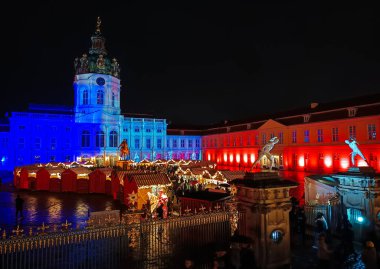 Berlin, Almanya - 30 Kasım 2025 Berlin 'deki Charlottenburg Sarayı' nda Noel Pazarı. Aydınlatılmış saray cephesinin akşam manzarası şenlik tezgahları, tatil ışıkları ve hareketli bir kalabalık.