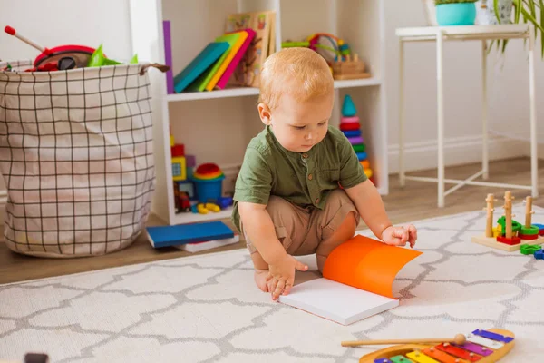 O bebê está olhando para um livro aberto na sala de jogos — Fotografia de Stock