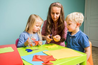Küçük çocuklar bir öğretmenle renkli bir poster yapıyorlar.
