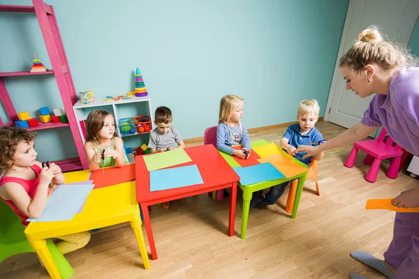 The tutor teaches kids how to cut out of colored paper — Stock Photo, Image