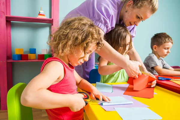 Little children and tutor cut out figures from colored paper — Stock Photo, Image