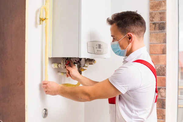 The plumber repairs a boiler in a medical mask