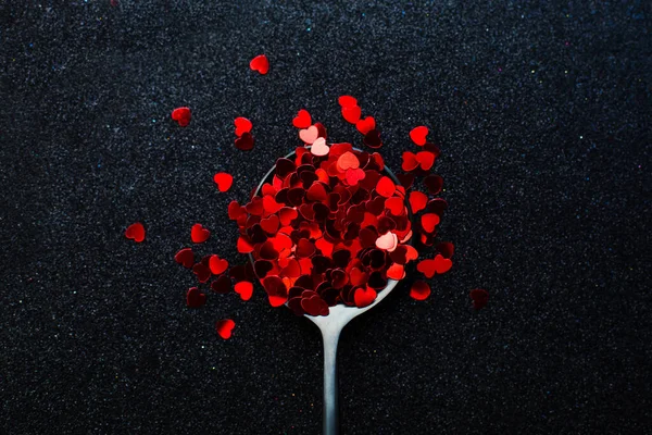Black spoon of red small hearts on the black sparkle back — Stock Photo, Image