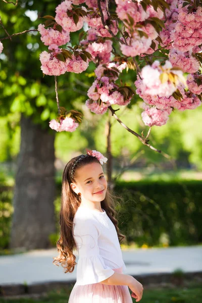 Het meisje staat onder de roze boom die bloeit — Stockfoto