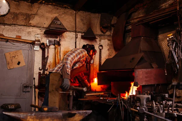 El herrero forja manualmente el metal fundido en el yunque en la herrería. — Foto de Stock