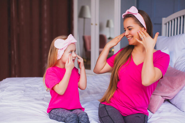 Girl and her mom sitting on the bed and make face care