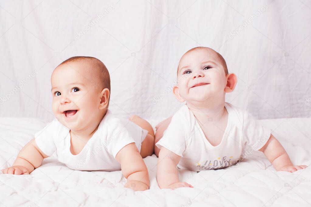 Two baby twins lying on the stomach at the white