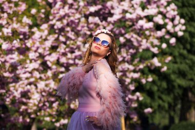 Kız çiçek açan pembe ağacın altında duruyor.