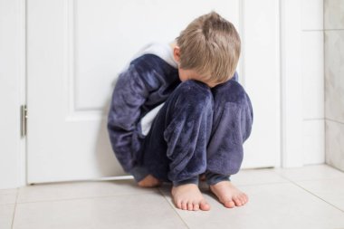 Üzgün çocuk yerde kapalı bir pozisyonda oturuyor.