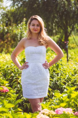 Beyaz elbiseli kadın çiçeklerin arasında poz veriyor.