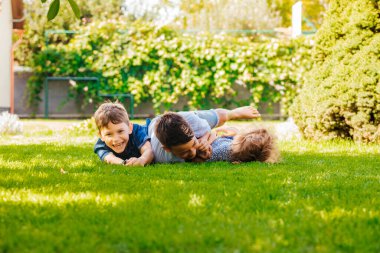 Yeşil çimlerin üzerinde yatan üç küçük çocuğun portresi.