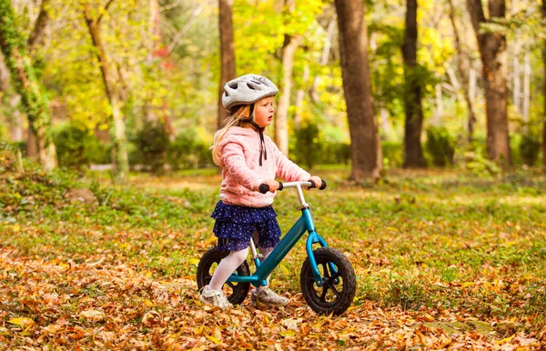 Lovely girl riding balance bike in atumn park