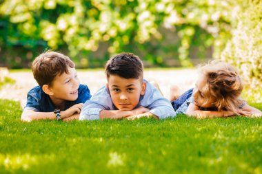 Yeşil çimlerin üzerinde yatan üç küçük çocuğun portresi.