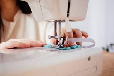 Profesyonel terzi koruyucu tıbbi maske dikiyor, yakından bakıyor.