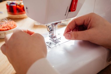 Eller dikiş makinesinin iğnesine iplik sokuyor.